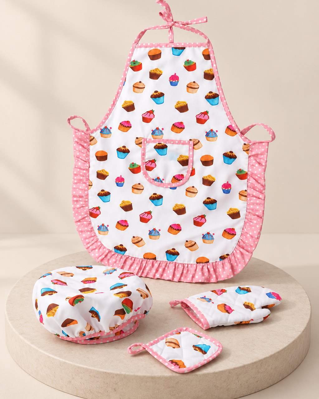 White cupcake-print kids' apron with pink frills, shown flat