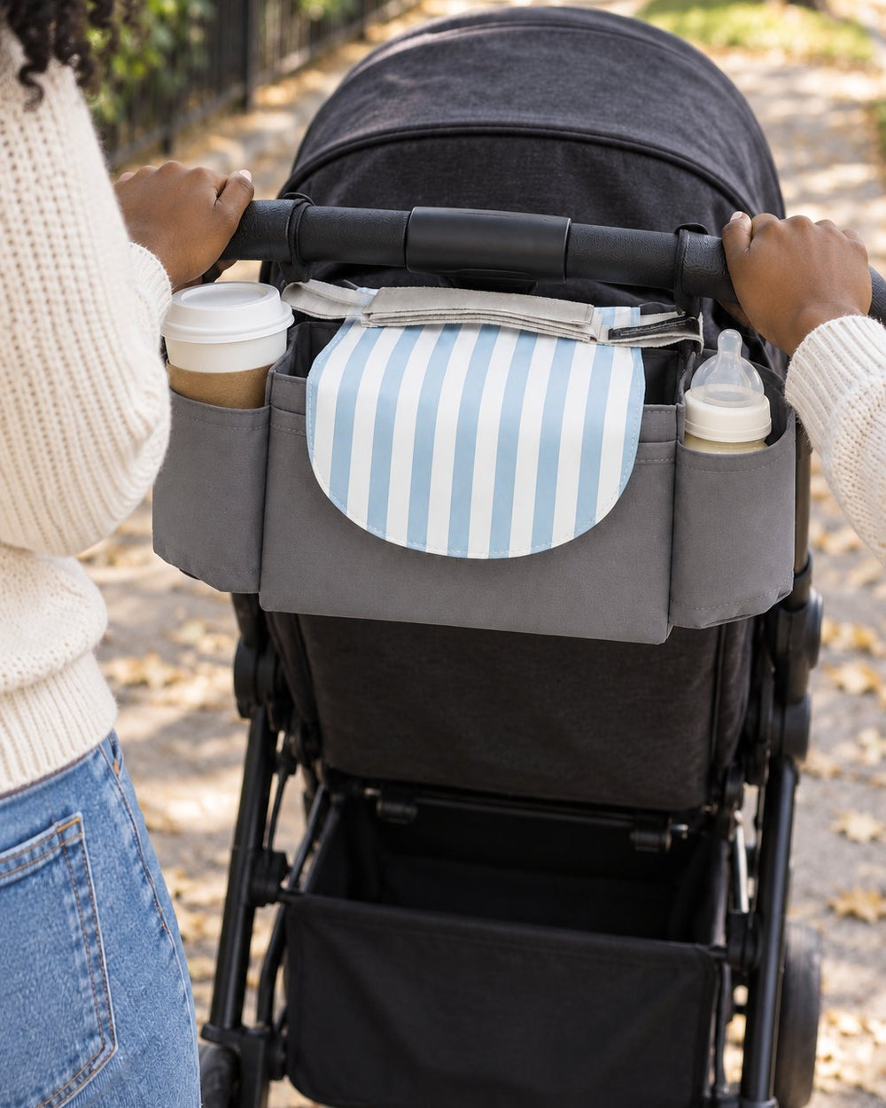 Organizer bag strapped across a stroller handlebar with a coffee cup in its side pocket