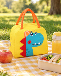 Dino lunch bag on a picnic blanket beside fruit and a drink bottle