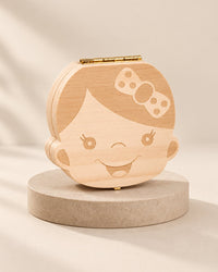Light wooden tooth box shaped like a smiling girl's face with a bow and a small brass clasp
