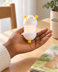 Adult hand holding the squashed-down caterpillar light beside a picture book