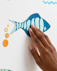 Hand smoothing a teal patterned fish decal onto a white wall
