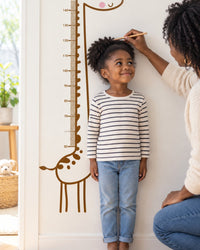 Child standing back against the giraffe decal while a parent marks their height