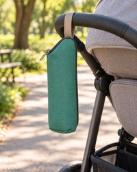 Green bottle bag hanging by its loop from a stroller handlebar in a park