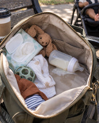 Damp diaper bag with a loose baby bottle lying among wet wipes and clothes