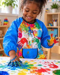 Child finger painting at a table wearing the paint-splash smock