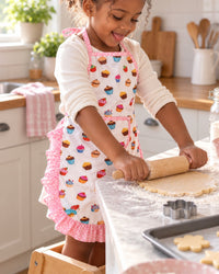 Child in the cupcake apron rolling cookie dough with the small wooden rolling pin