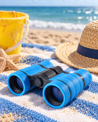 Blue kids' binoculars on a beach towel with a bucket and sun hat