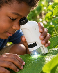 Child holding the white pocket microscope over a leaf in a garden, eye to the eyepiece