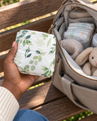 The cover folded small in one hand next to a diaper bag