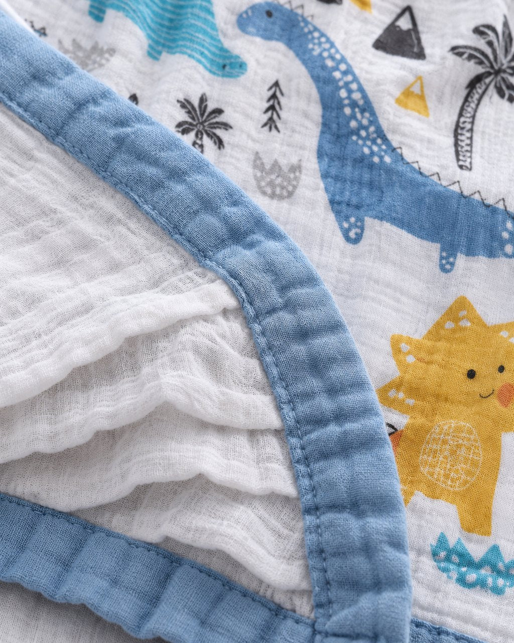 Close-up of the blanket corner showing the crinkly muslin layers and the blue bound edge