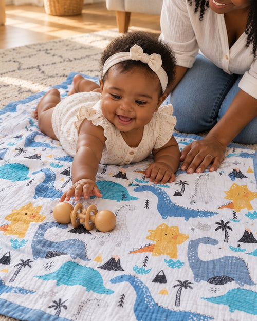 Smiling baby on her tummy on the dinosaur muslin blanket on a living-room rug, her mother kneeling beside her