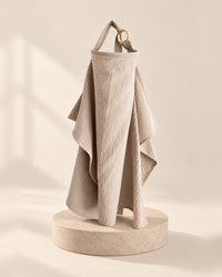 Oat-coloured crinkly muslin nursing cover hanging from its neck strap