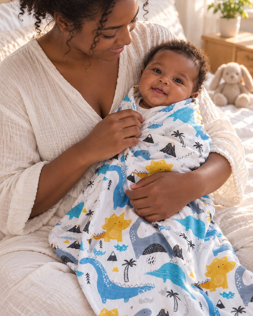 Mother wrapping her awake newborn in the dinosaur muslin swaddle on her lap