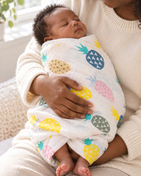 Parent holding a newborn snugly swaddled in the pineapple muslin