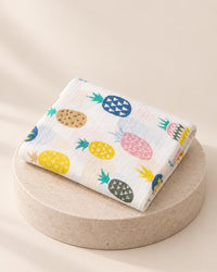 Folded white muslin swaddle printed with pastel pineapples