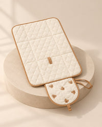 Cream quilted changing pad laid open, with embroidered bears and tan piping