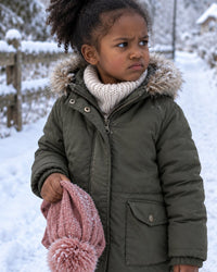 Child with red cold ears holding a pulled-off hat on a winter path