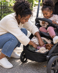 Parent crouching to dig through a cluttered stroller basket for keys