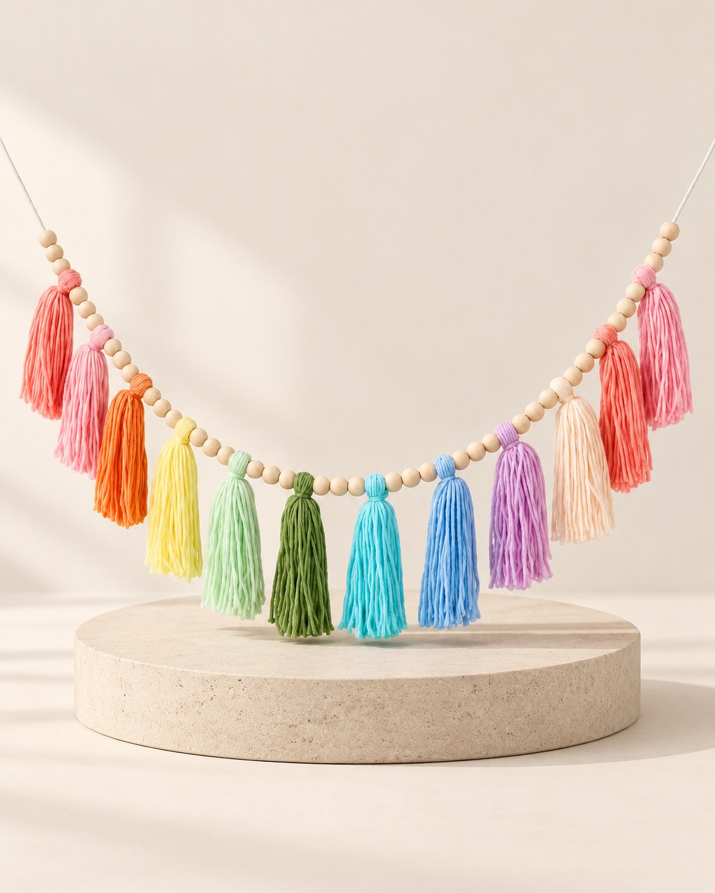 Soft rainbow yarn tassels strung between natural wooden beads on a white wall