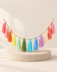 Soft rainbow yarn tassels strung between natural wooden beads on a white wall