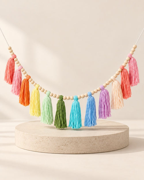Soft rainbow yarn tassels strung between natural wooden beads on a white wall