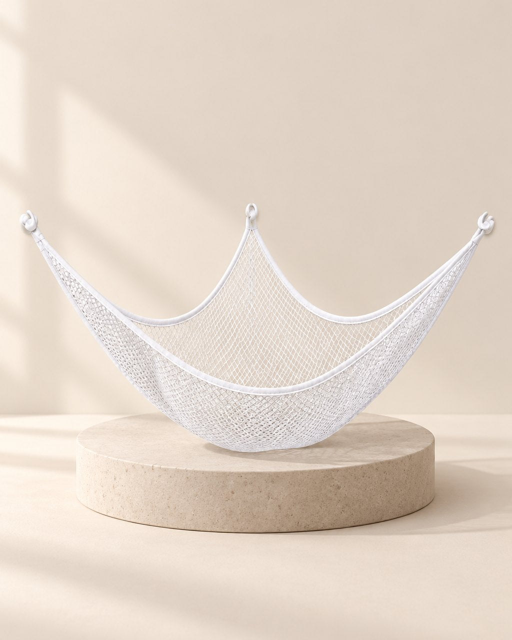White mesh triangle hammock full of stuffed animals strung across a room corner
