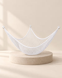 White mesh triangle hammock full of stuffed animals strung across a room corner