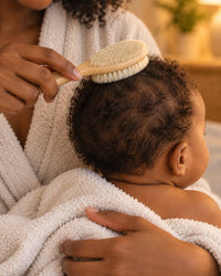 Parent gently brushing a baby's fine hair with the soft goat-hair brush