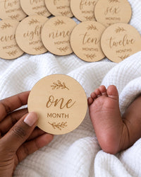 Wooden disc held in a parent's hand beside a baby's tiny foot